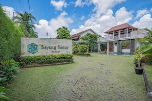 A resort entrance with a sign, paved walkway, and greenery.
