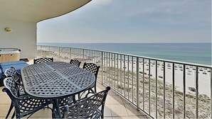 Un balcone con tavolo e sedie, con vista su una spiaggia e auto parcheggiate.