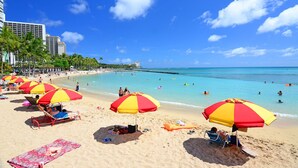 Ein Strand mit mehreren Sonnenschirmen, sandigem Ufer und klarem, blauem Wasser.