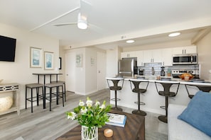 Una cocina moderna con armarios blancos, electrodomésticos de acero inoxidable y una isla central con taburetes de bar.