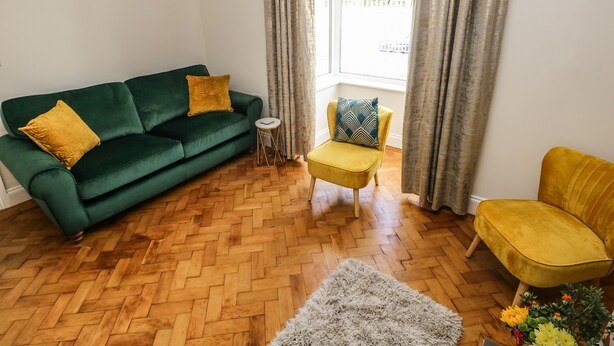 A living room with a green sofa, a yellow armchair, and a small round table. - Larkhill (Tenby)