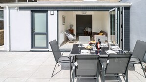 Um pátio com uma mesa posta para refeições, cadeiras e vista para o interior da casa.
