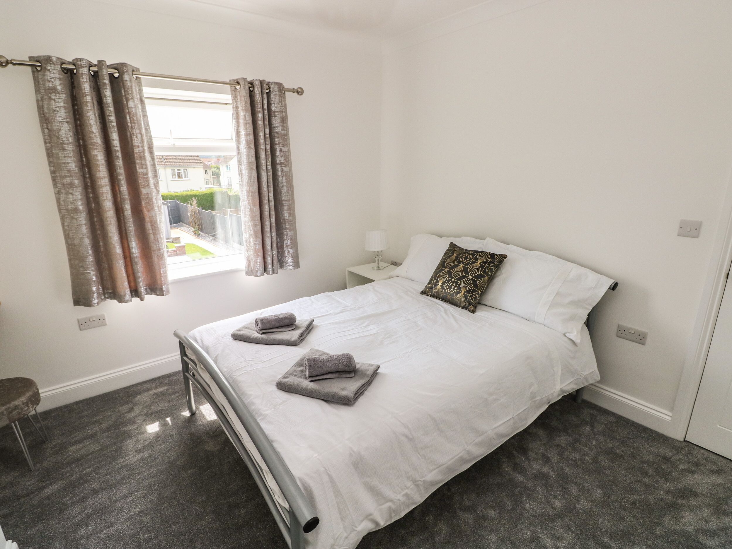 A bedroom with a bed, a nightstand, a lamp, and a window with curtains.