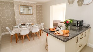 Uma cozinha moderna com área de refeições, com bancada de mármore, forno embutido e mesa de jantar com cadeiras brancas.
