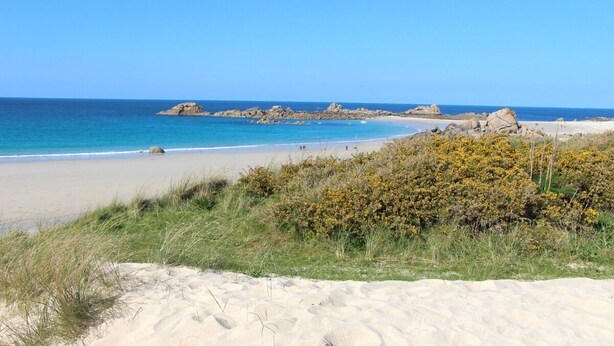 A beach with clear blue water, sandy shore, and rocky outcrops in the distance.