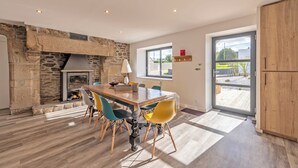A dining area with a stone fireplace, a wooden table, and colorful chairs.