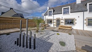 A modern house with a wooden deck, a small garden area with gravel and plants, and a wooden fence.