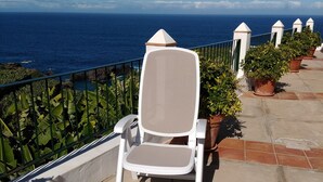 Ein weißer Stuhl mit Netzlehne auf einem Balkon mit Blick aufs Meer.