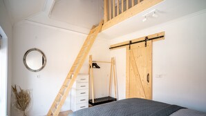 A bedroom with a loft bed, wooden ladder, and a sliding barn door.