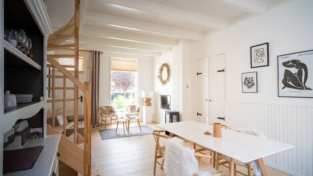 A modern kitchen with wooden cabinets, a white countertop, and a wooden staircase leading to a dining area.