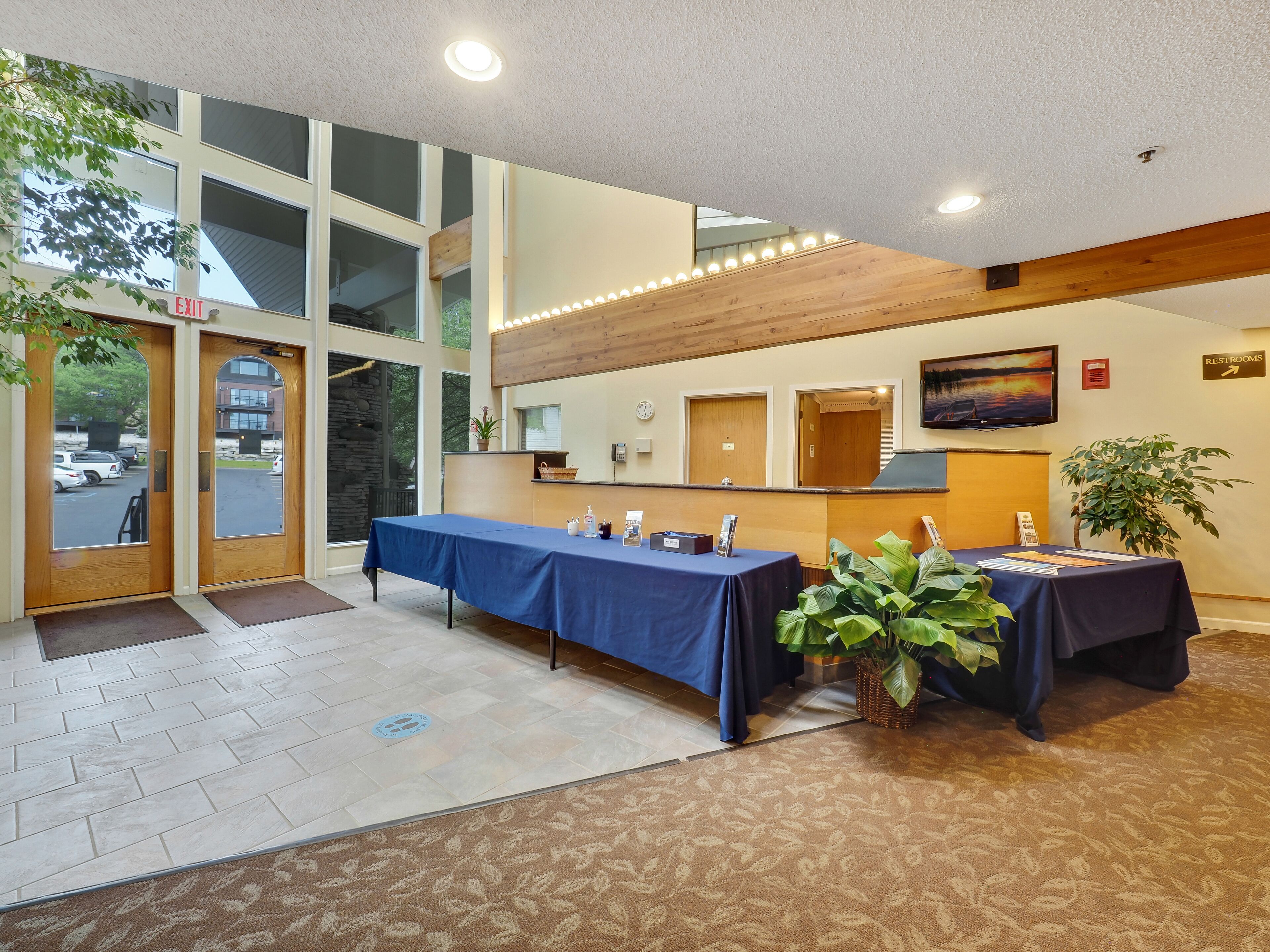 A conference room with a long table, two chairs, a plant, and a TV on the wall.