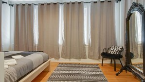 Ein Schlafzimmer mit einem Bett, einem Sessel, einem Spiegel und einem gemusterten Teppich.