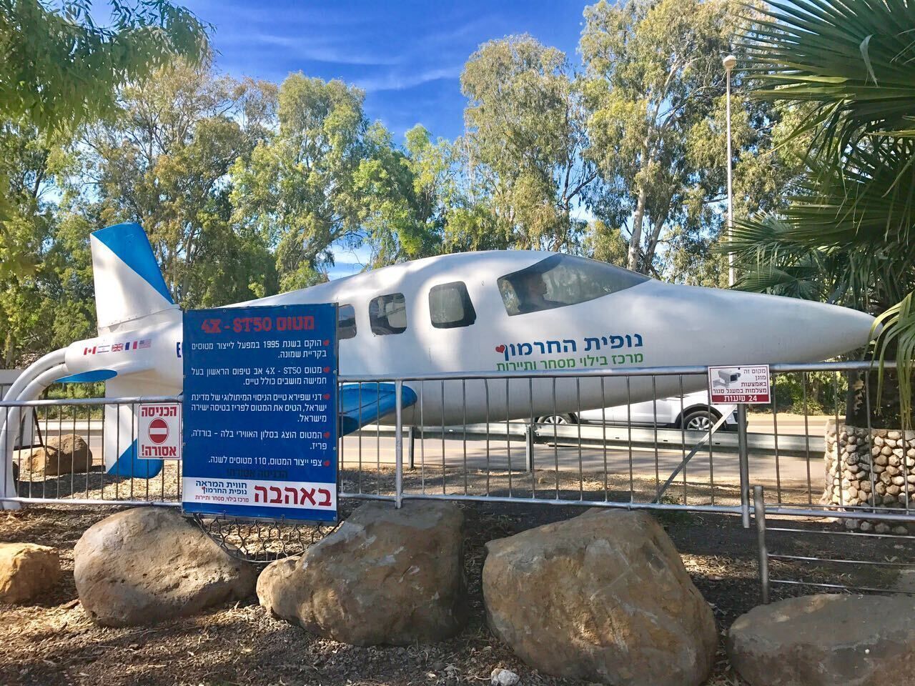 Ein kleines Flugzeug steht draußen vor Bäumen und Felsen, mit einem Schild in Hebräisch.