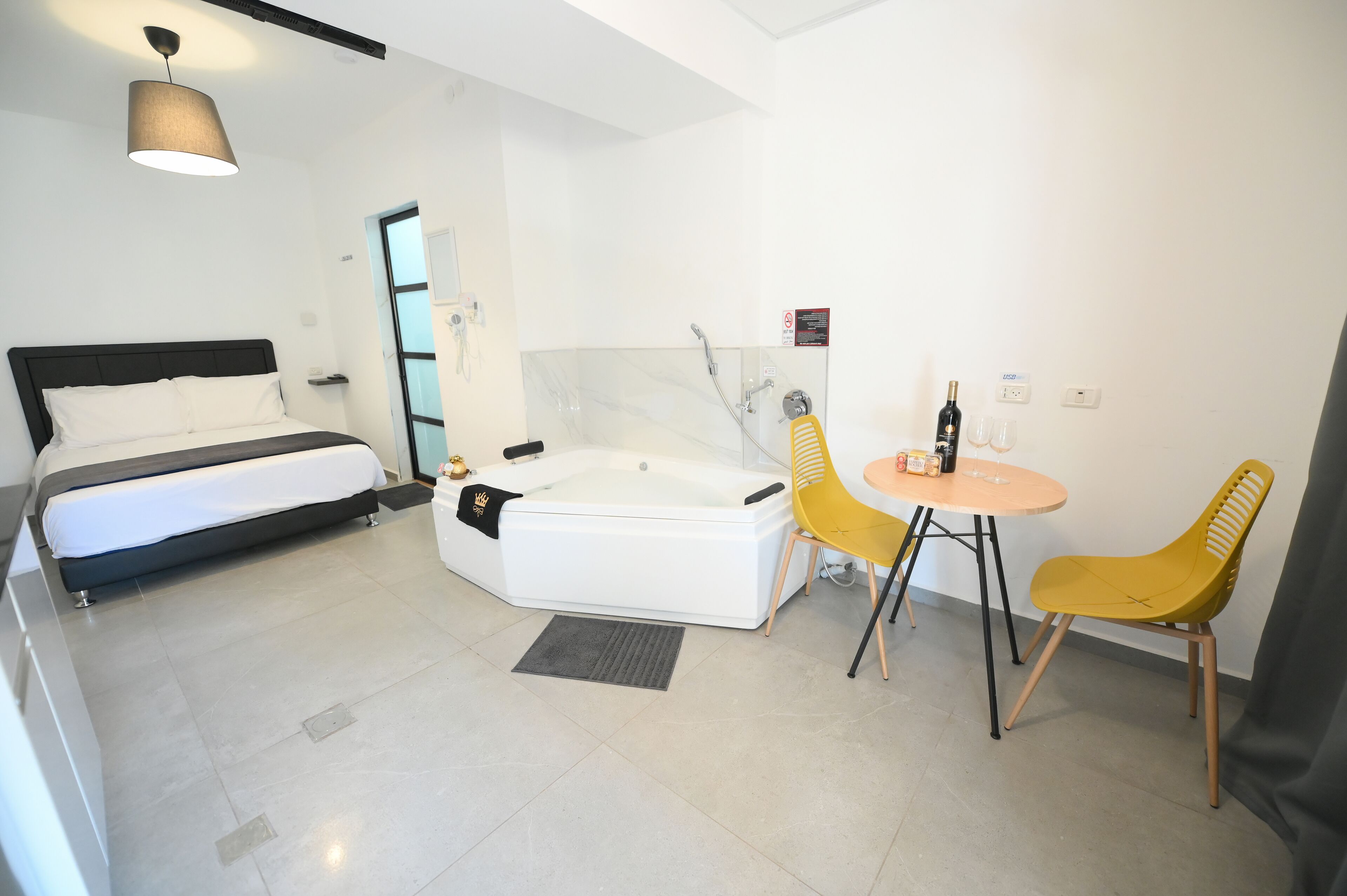Ein modernes Hotelzimmer mit Bett, Whirlpool und einer kleinen Essecke mit gelben Stühlen.