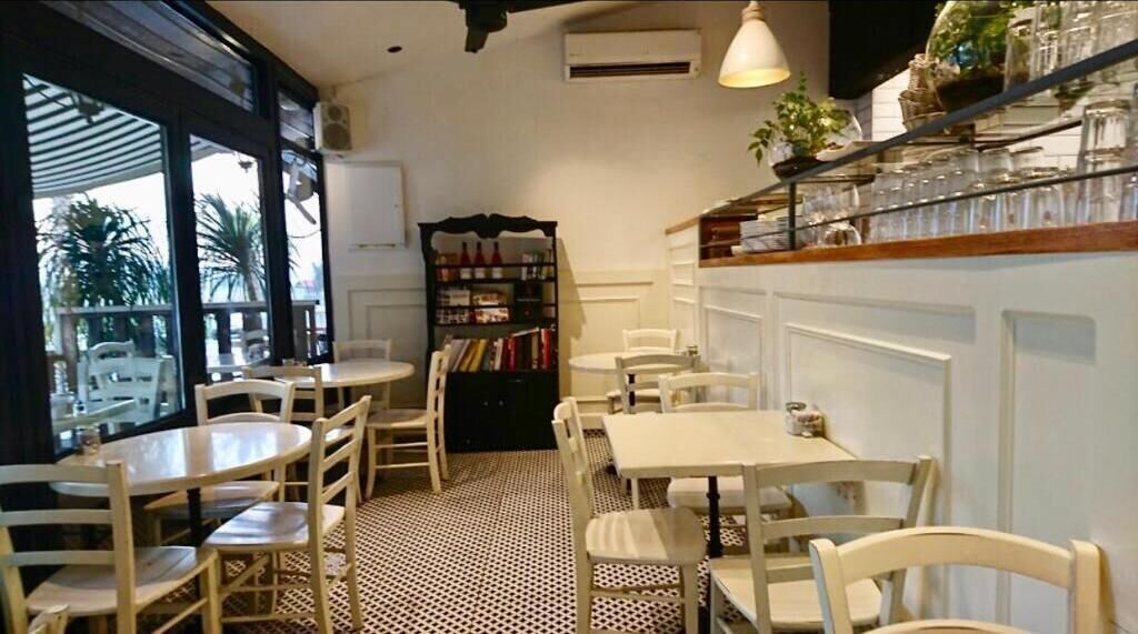 Un café chaleureux avec des tables et des chaises rondes, une bibliothèque et une vue dégagée grâce à de grandes fenêtres.