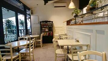 Un café chaleureux avec des tables et des chaises rondes, une bibliothèque et une vue dégagée grâce à de grandes fenêtres.