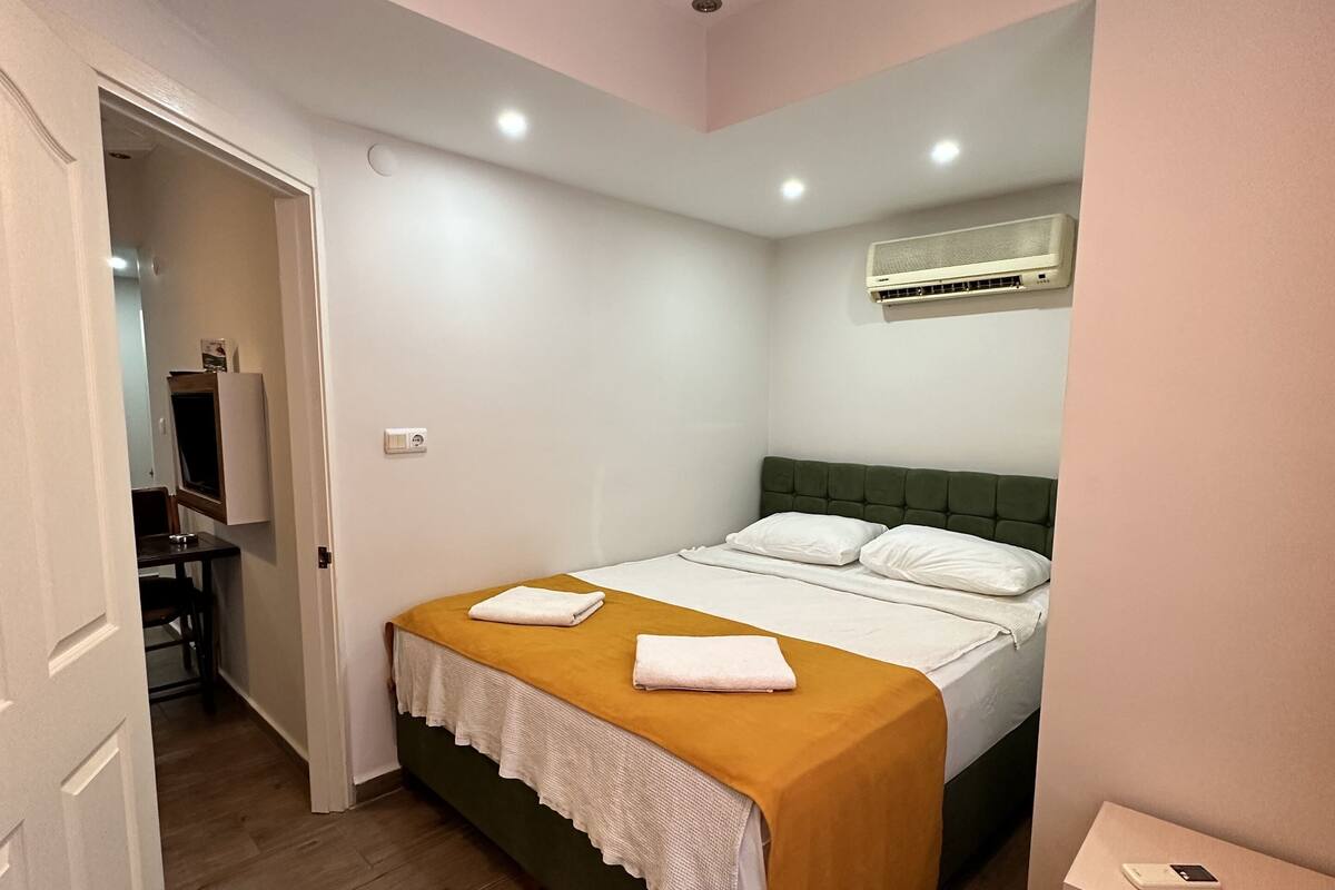 A bedroom with a bed, a bedside table, a chair, and a desk.