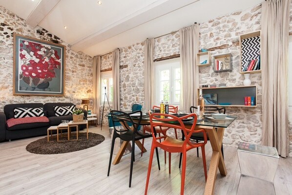 A living room with a stone wall, a sofa, a dining table with chairs, and a bookshelf.