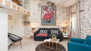 A spacious living room with a stone wall, a black sofa with patterned cushions, a blue armchair, a black chair, and a coffee table with a plant. - Superb loft apartment in the heart of old Antibes 3mns from the beach (Antibes)