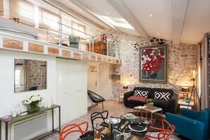 A spacious living area with a high ceiling, stone walls, and a mezzanine level.