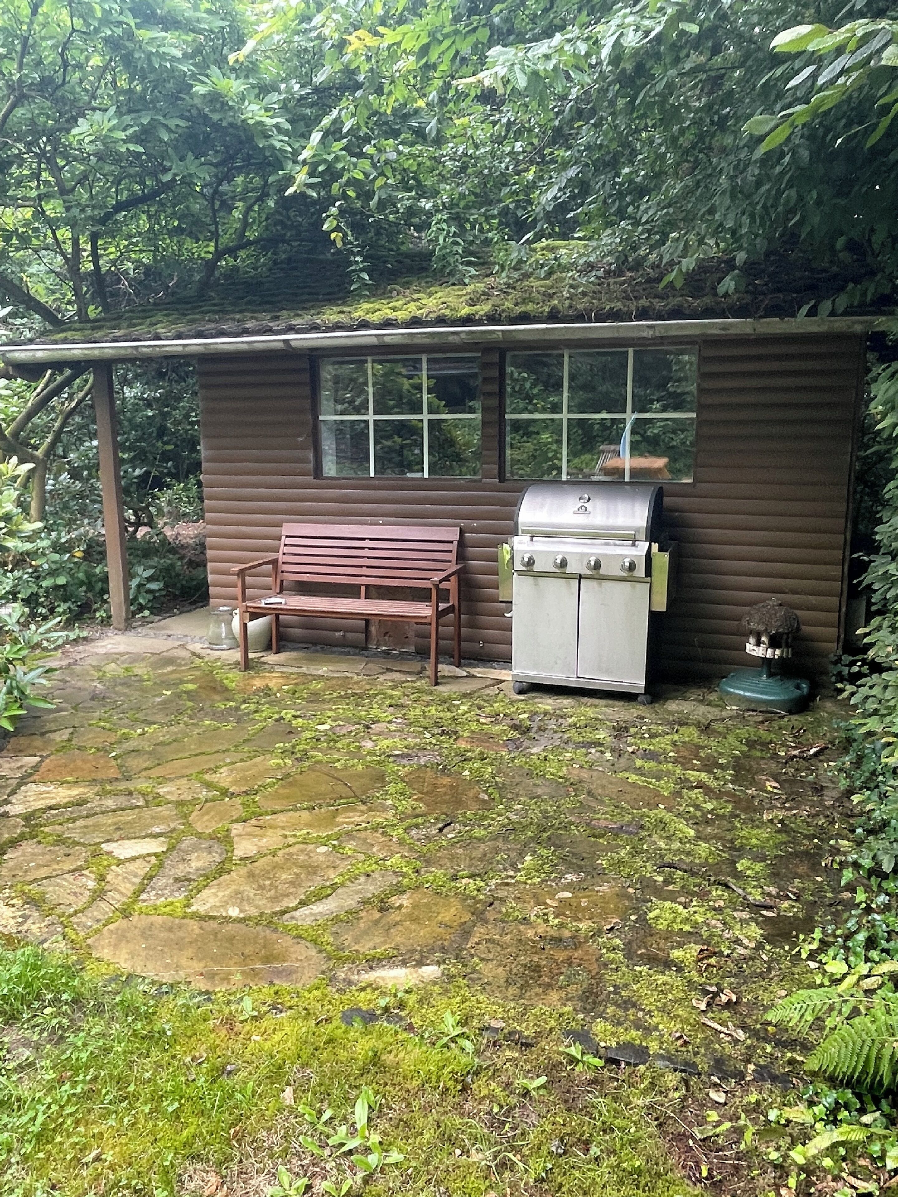 A small wooden cabin with a grill and a bench outside.