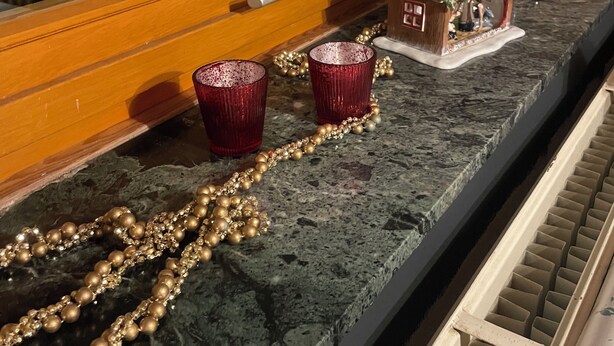 Un comptoir de cuisine orné d’une maquette de maison décorative, de deux tasses rouges et d’un collier doré orné de perles.