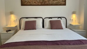Un lit bien fait, avec deux oreillers, une table de chevet sur laquelle se trouve une lampe, et une œuvre d’art encadrée au-dessus du lit.