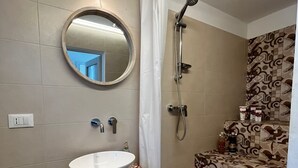Une salle de bain avec un miroir rond, un lavabo, une douche et des carreaux décorés.