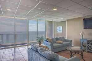 Relax in a spacious living area with a high ceiling, featuring a large sliding glass door leading to a balcony with ocean views.