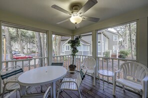 Eine überdachte Terrasse mit Deckenventilator, weißen Gartenmöbeln und Blick auf benachbarte Häuser.