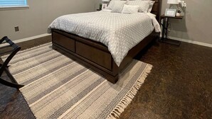 A bedroom with a large bed, a nightstand, a wall-mounted mirror, and a window with blinds. - [SU 922-3] Campus-close 2 bedroom luxury (Norman)