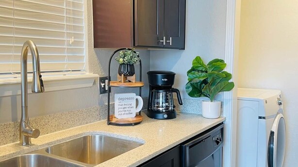 A kitchen with a double sink, dark cabinets, a coffee maker, a potted plant, and a washing machine. - [SU 922-3] Campus-close 2 bedroom luxury (Norman)