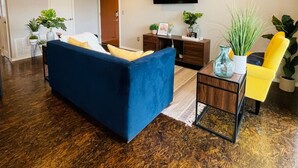 A living room with a blue sofa, a yellow chair, a wooden coffee table, and a TV mounted on the wall. - [SU 922-3] Campus-close 2 bedroom luxury (Norman)