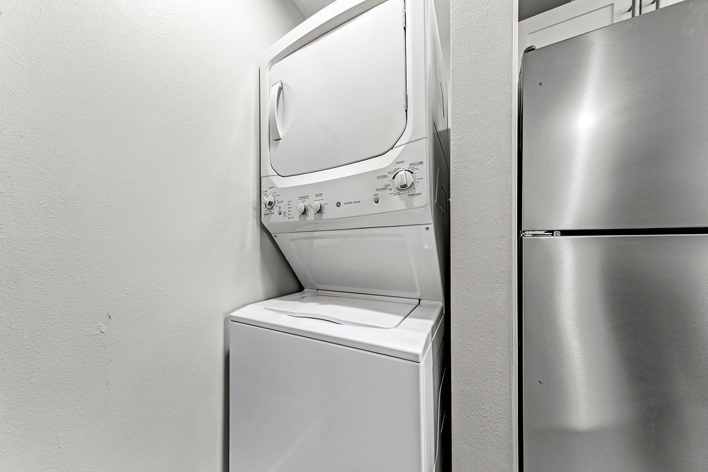 A compact laundry room with a front-loading washer and a stainless steel refrigerator.