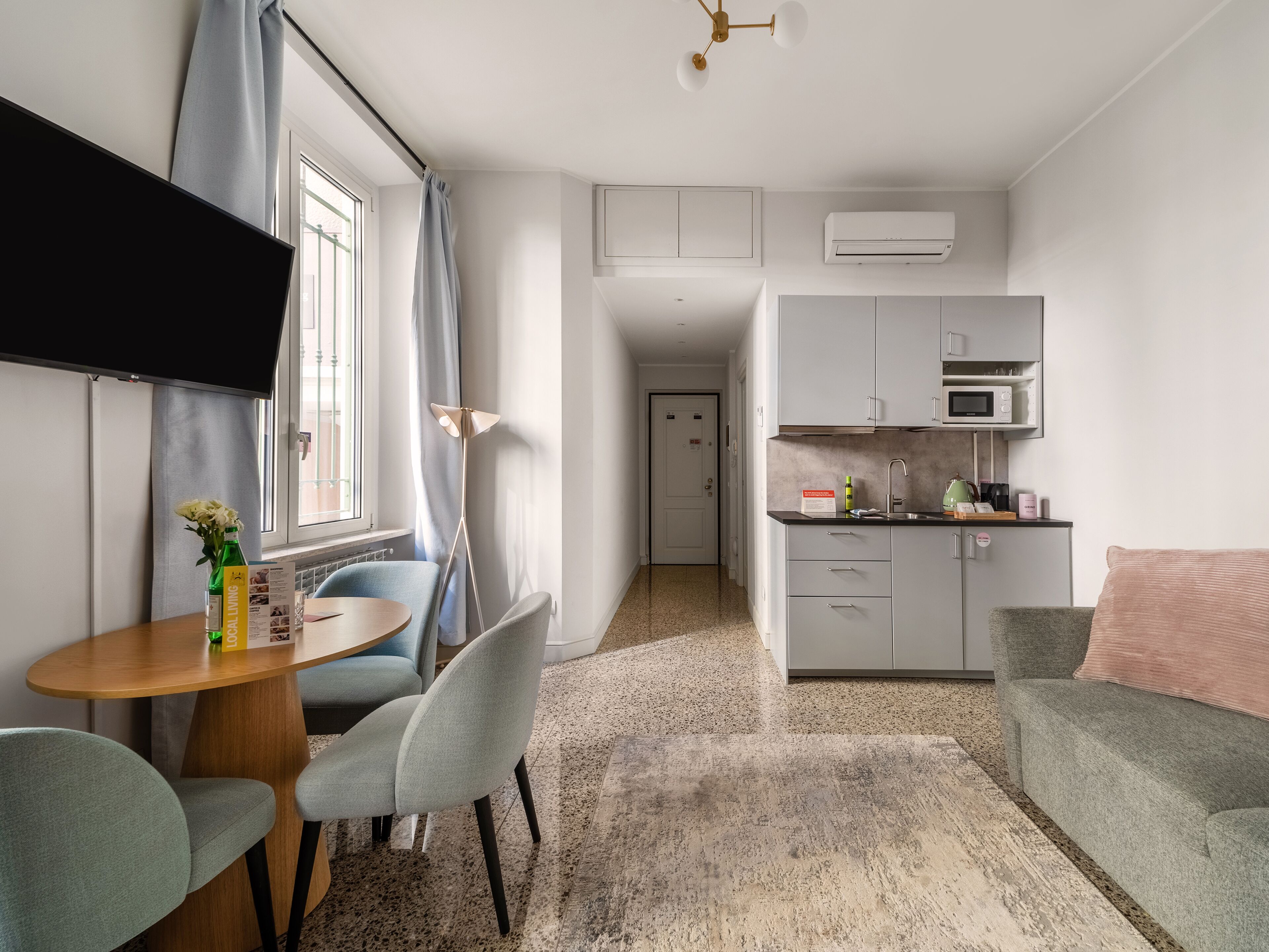 A compact living space with a dining area, kitchenette, and a TV mounted on the wall.