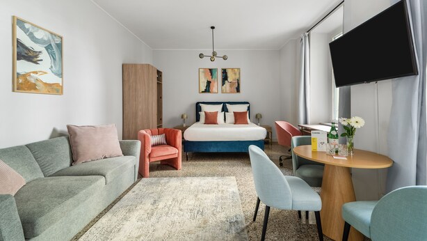 Een moderne hotelkamer met een bed, een bank, een stoel, een kleine tafel en een televisie.