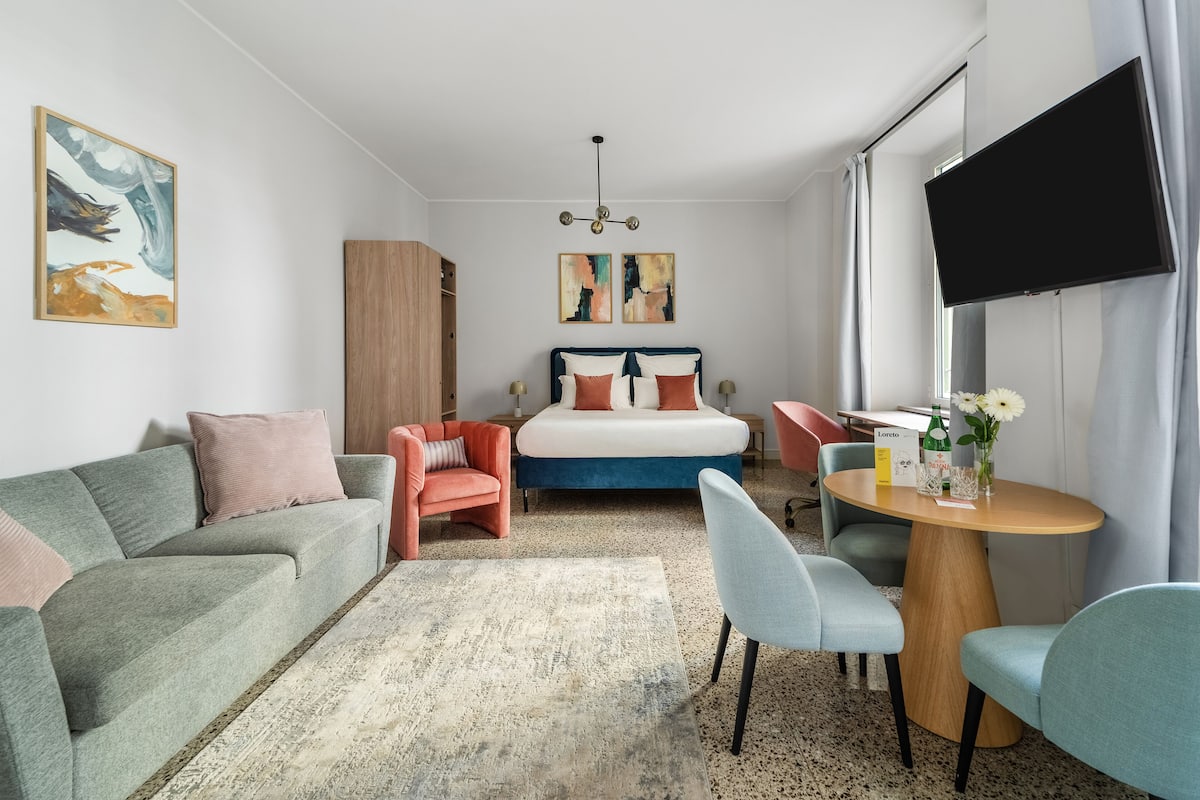 Una habitación de hotel moderna con cama, sofá, sillón, mesita y televisor.
