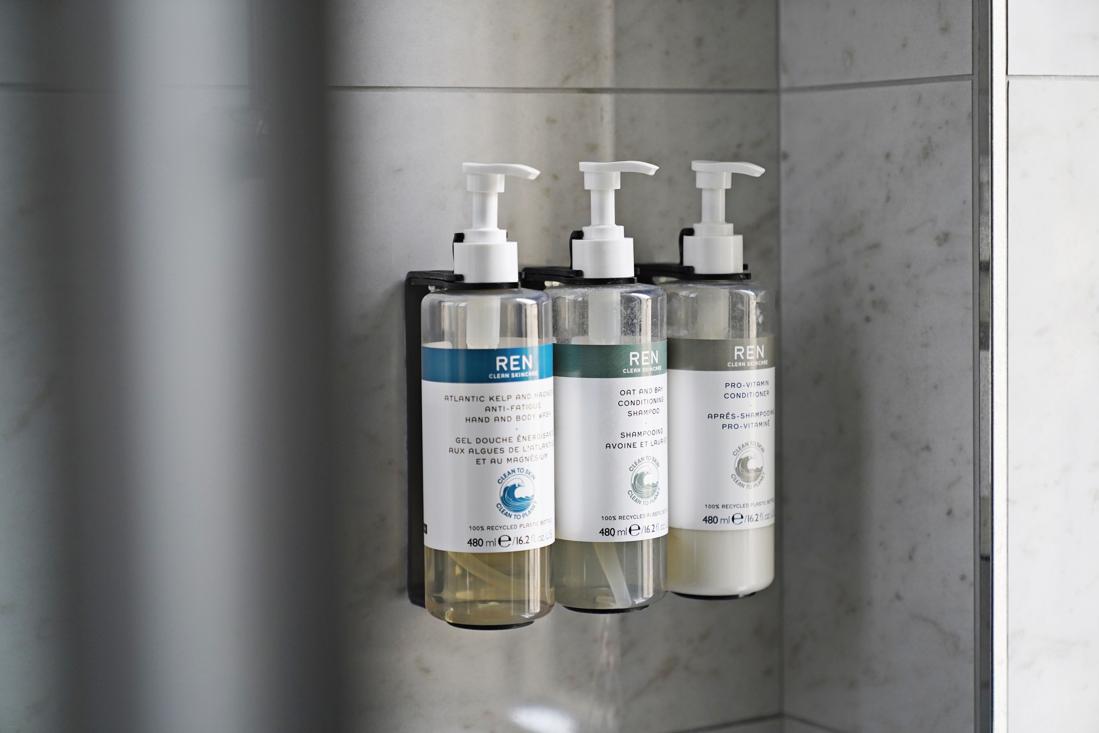 Trois flacons de produits de soins pour la peau de la marque REN sont accrochés à un mur.