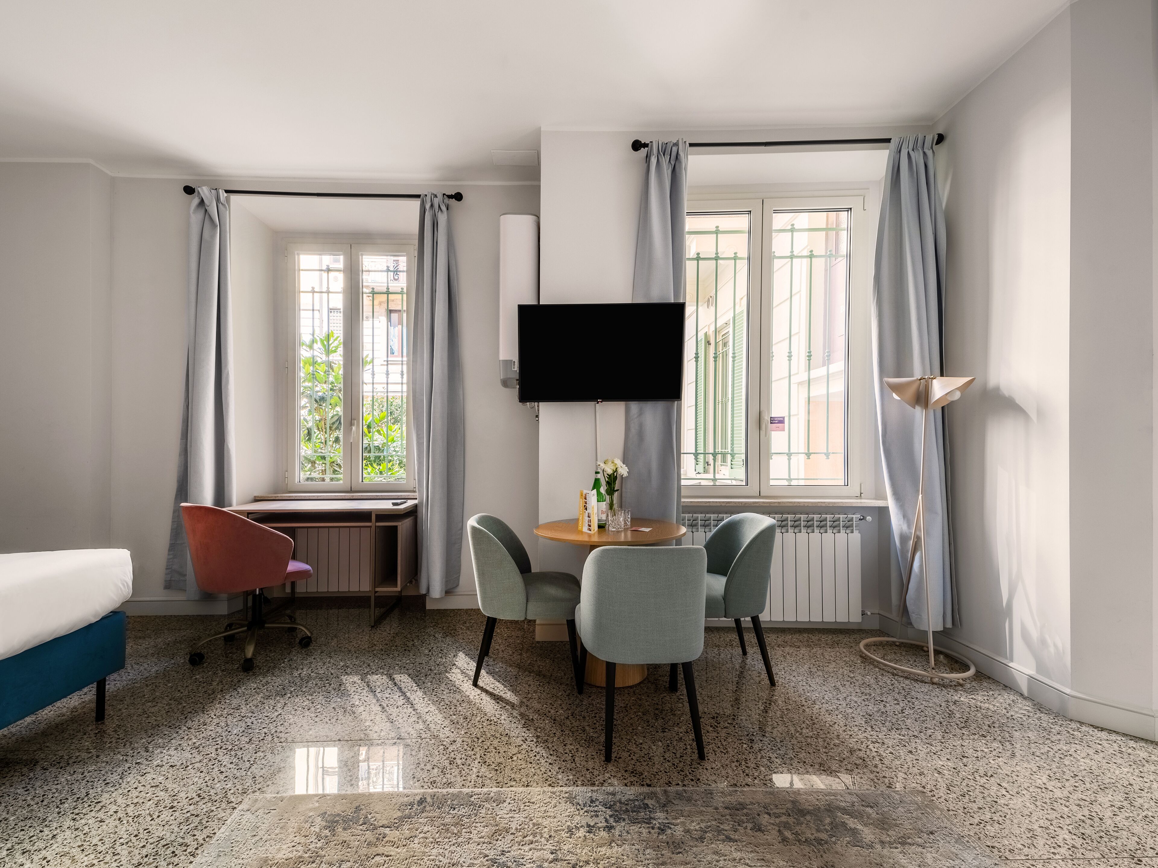 A hotel room with a bed, a desk, a TV, a chair, a table, and a floor lamp.