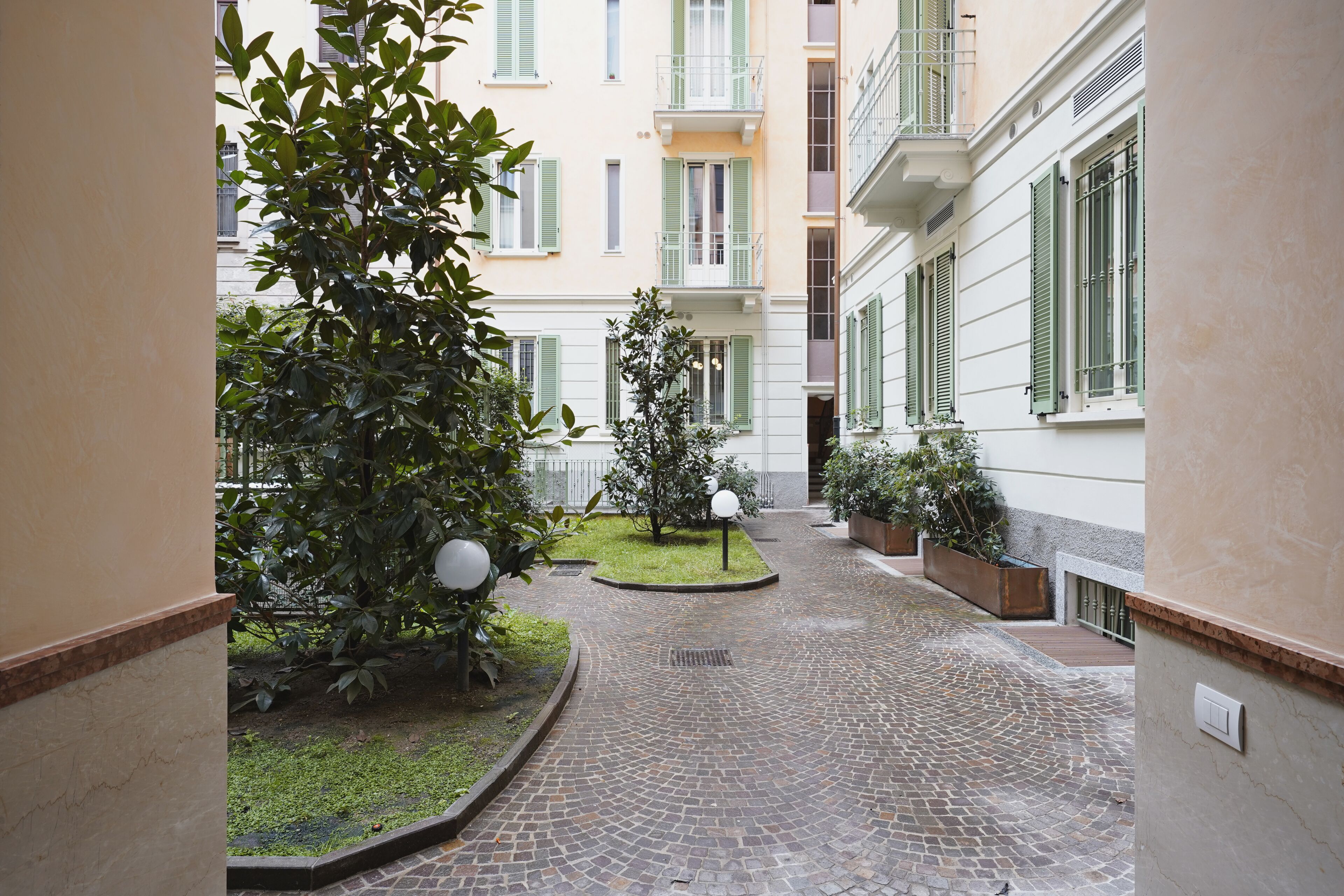 Ein Innenhof mit Kopfsteinpflasterweg, Grünpflanzen und einem kleinen Gartenbereich.