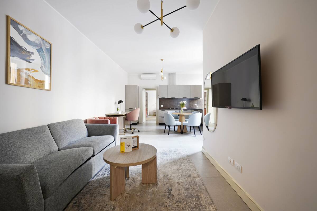 Una sala de estar moderna con un sofá gris, una mesa de centro redonda de madera y un televisor de pantalla plana montado en la pared.