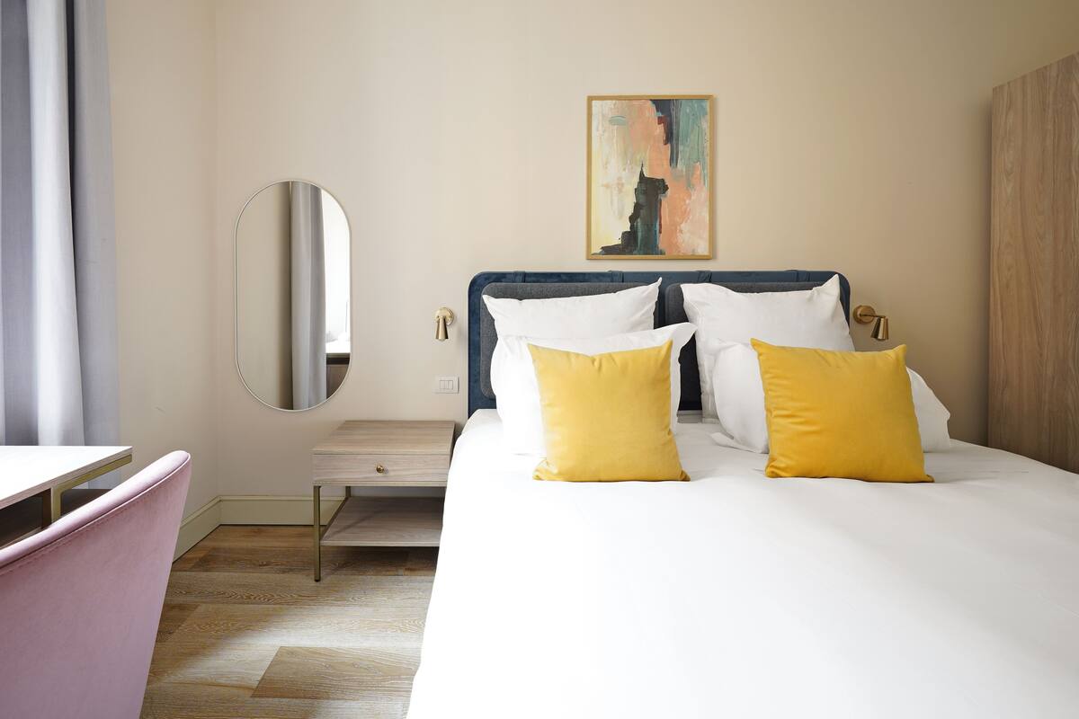 Una habitación de hotel con cama, mesita de noche, silla y un cuadro en la pared.