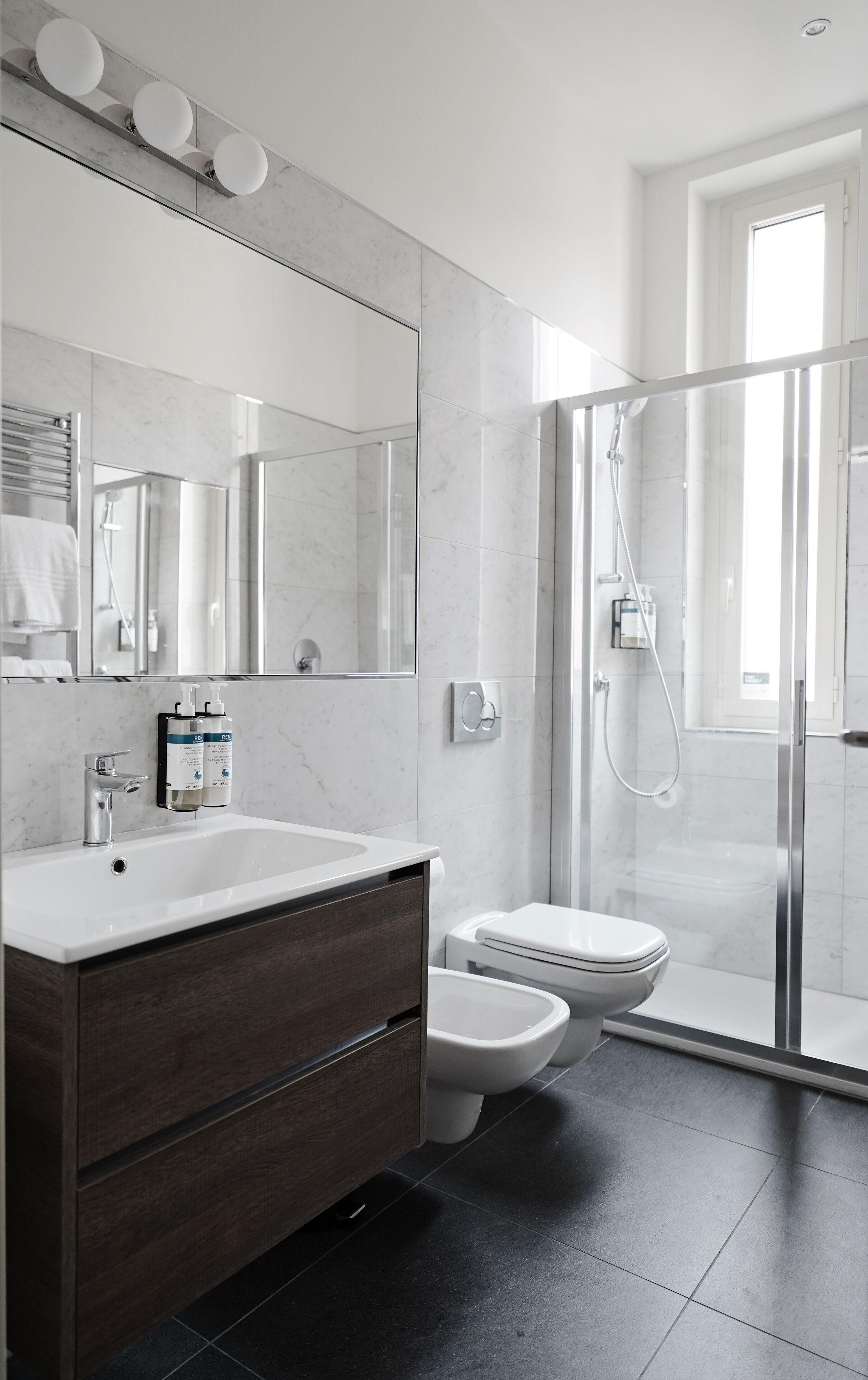 A modern bathroom with a large mirror, a white sink, a dark wooden vanity, a toilet, and a glass-enclosed shower area.