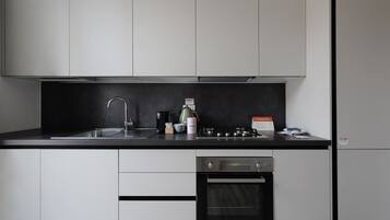 A modern kitchen with white cabinets, a black countertop, a stainless steel sink, a coffee maker, a kettle, and a built-in oven.