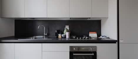 A modern kitchen with white cabinets, a black countertop, a stainless steel sink, a coffee maker, a kettle, and a built-in oven.