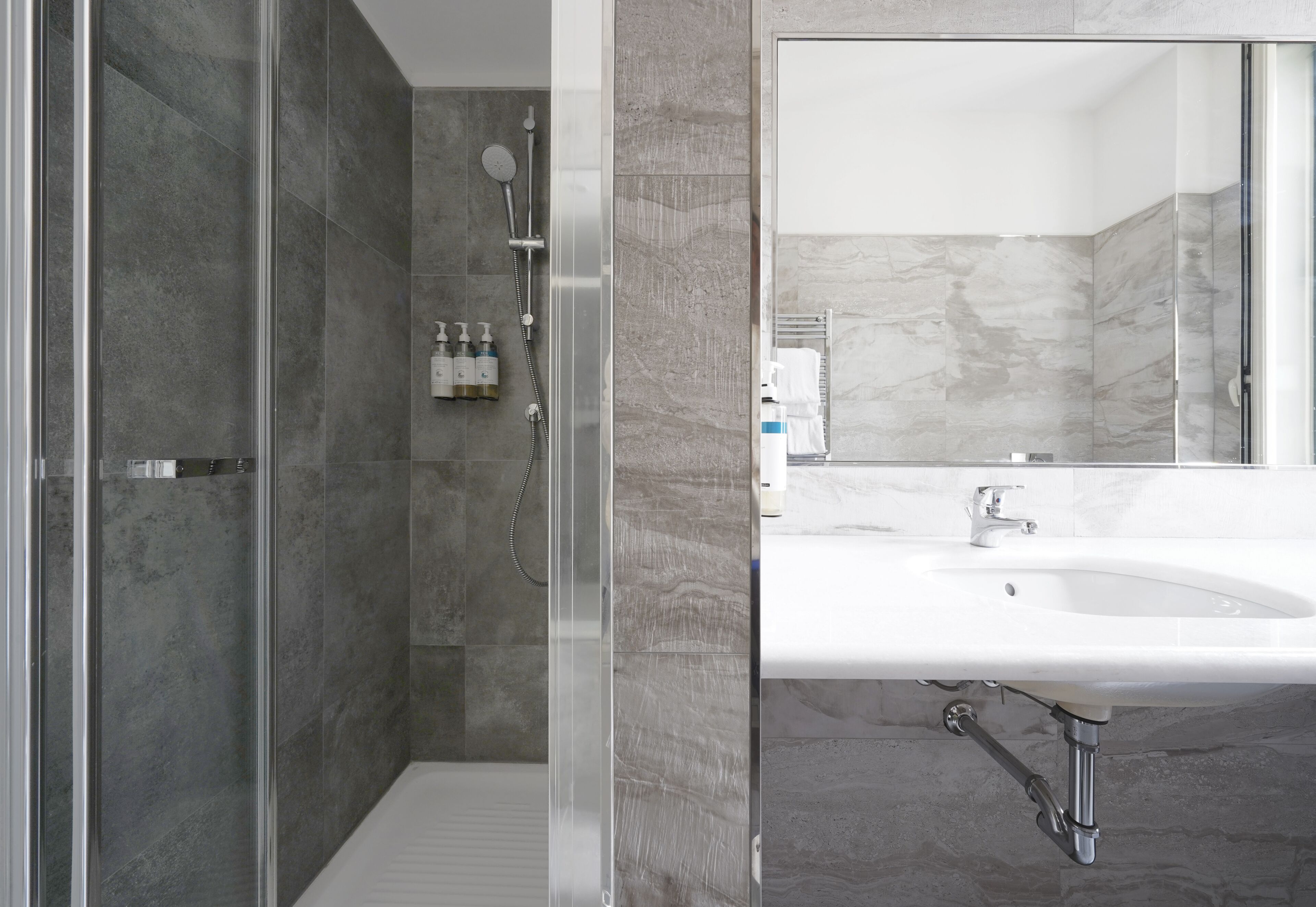 Een moderne badkamer met een douche met glazen wand, een grote spiegel en een witte wastafel.