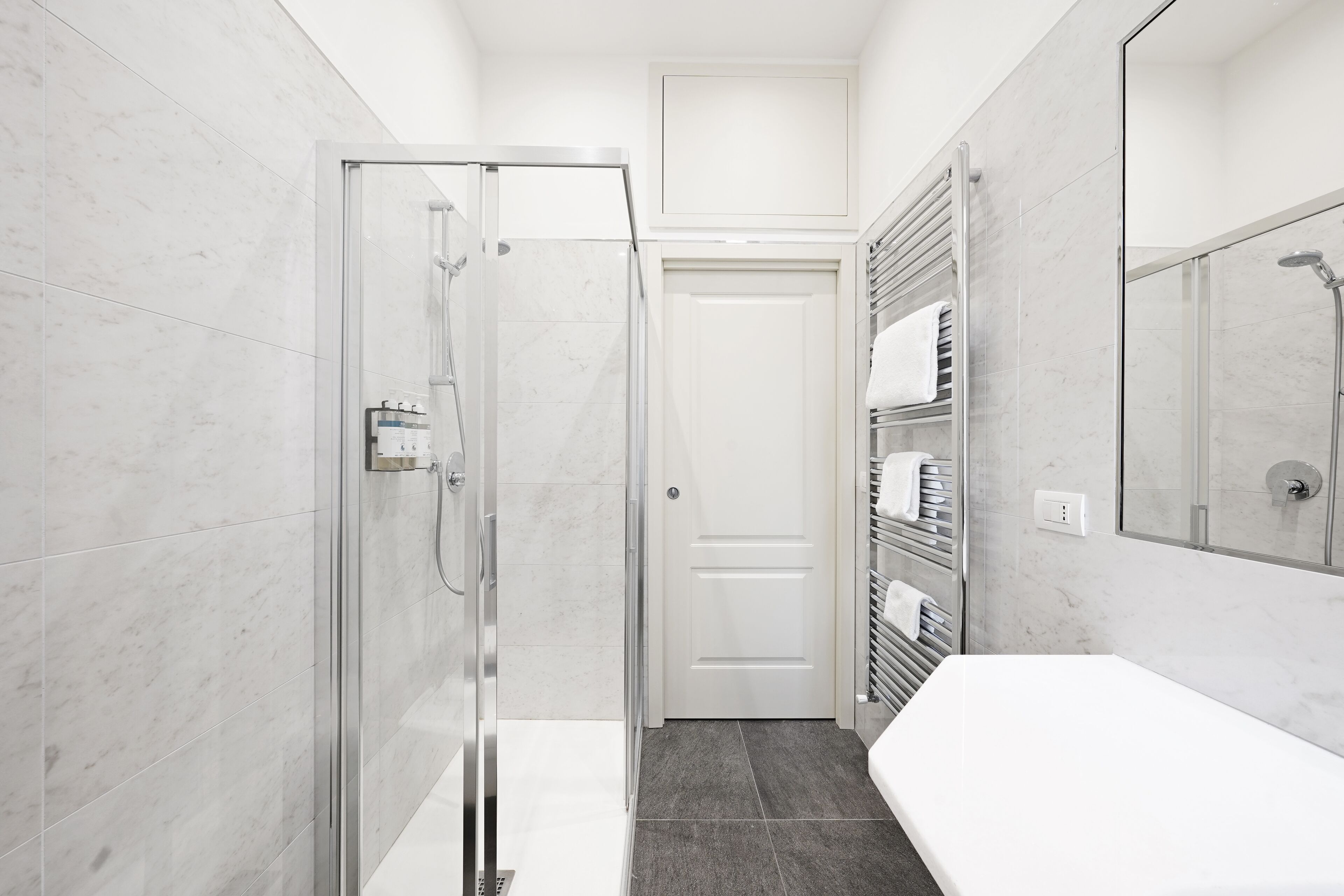 A modern bathroom with a glass shower enclosure, a white sink, and a towel rack.