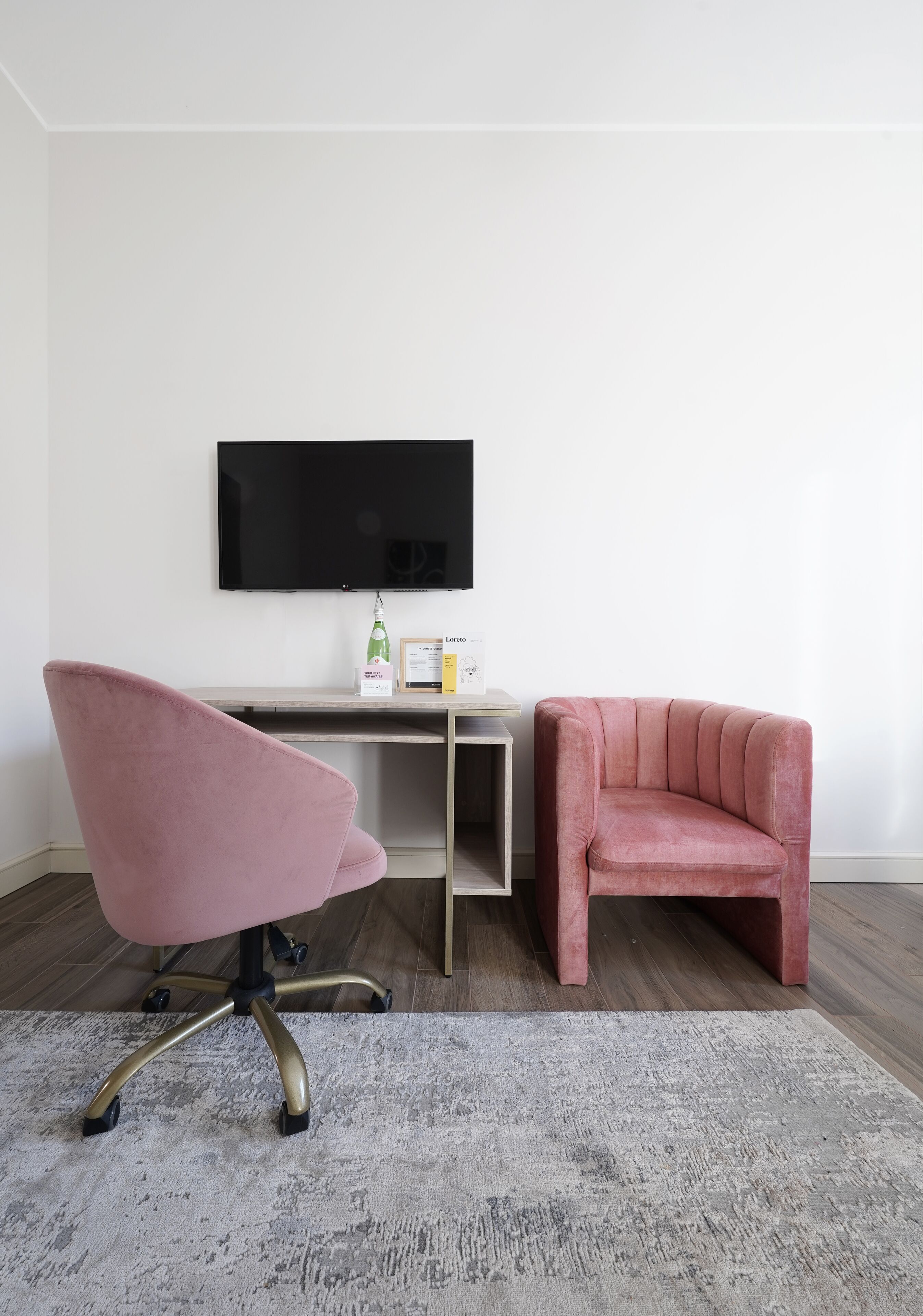 Een moderne kamer met een bureau, een roze stoel, een televisie en een klein tafeltje met spullen erop.