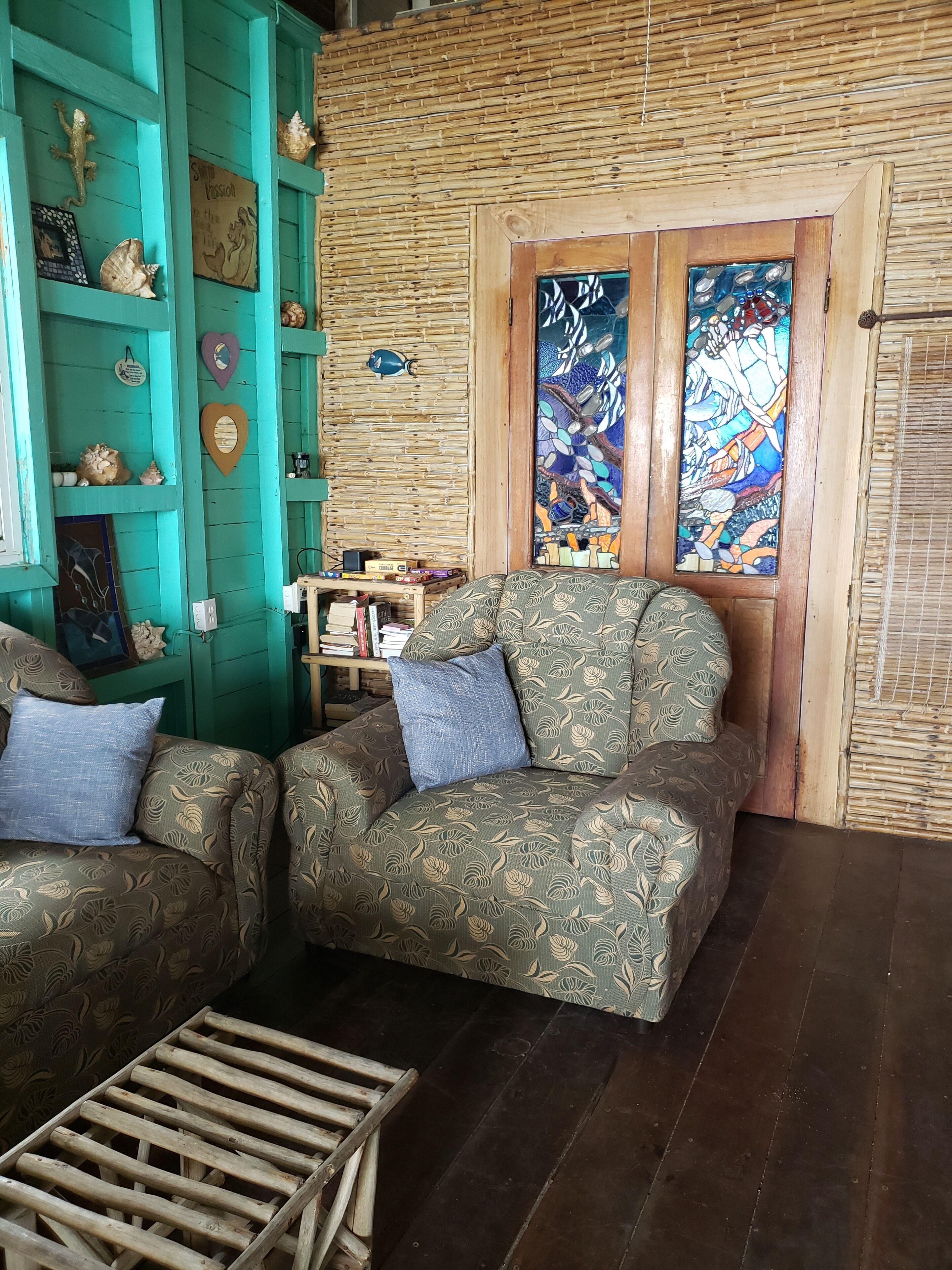 A cozy living room with two patterned sofas, a wooden coffee table, and a wall decorated with shells and a mosaic.