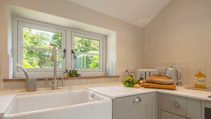 A modern kitchen with a white sink, double sink, and a window with a view of greenery. - Willow Cottage (SC), South Creake, Norfolk (South Creake)